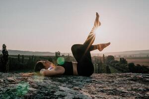 Fitness woman. Well looking middle aged woman with long hair, fitness instructor in leggings and tops doing stretching and pilates on the rock near forest. Female fitness yoga routine concept. photo