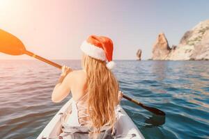 mujer en kayac espalda vista. contento joven mujer en Papa Noel sombrero flotante en kayac en calma mar. verano fiesta vacaciones y alegre hembra personas relajante teniendo divertido en el bote. foto