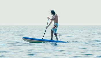 Man Sup Sea. Strong athletic man learns to paddle sup standing on board in open sea ocean on sunny day. Summer holiday vacation and travel concept. Aerial view. Slow motion photo