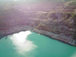 Aerial top view on opencast mining quarry with flooded bottom, turquoise surface of the lake. Quarry pond overgrown with green plants and clear turquoise water photo