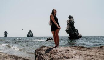 mujer verano viaje mar. contento turista en sombrero disfrutar tomando imagen al aire libre para recuerdos. mujer viajero posando en el playa a mar rodeado por volcánico montañas, compartiendo viaje aventuras viaje foto