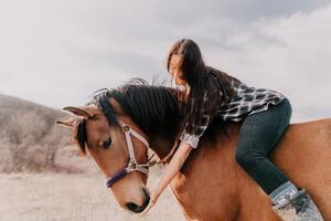 joven contento mujer en sombrero con su caballo en noche puesta de sol ligero. al aire libre fotografía con Moda modelo muchacha. estilo de vida humor. concepto de al aire libre equitación, Deportes y recreación. foto