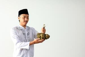 musulmán asiático hombre vistiendo blanco camisa baju koko y negro tapas kopyah participación ketupat arroz pasteles foto