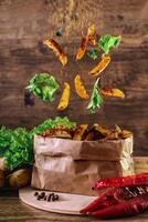 Flying slices of baked potato on wooden background. Lettuce, paprika, parsley. Fastfood. With spices. photo