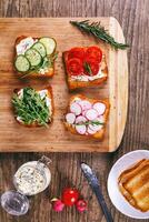 Four sandwiches with fresh vegetables, tomatoes, cucumbers, radish and arugula on a wooden background. Homemade butter and toast. Top view. photo
