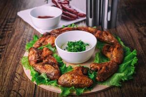 delicious grilled chicken wings with garlic and tomato sauce with lettuce on a round board on wooden rustic background photo