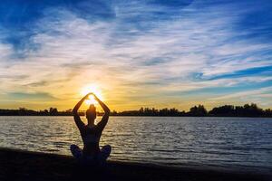 Young woman doing yoga exercises on the lake beach at sunset photo