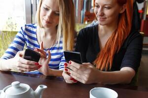 Two women having fun at the cafe and looking at smart phone. photo