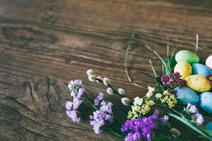 Easter background. Bright colorful eggs in nest with spring flowers over wooden dark background. Selective focus with copy space. photo