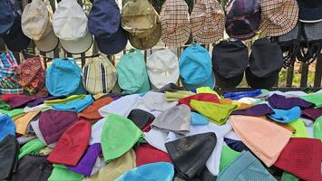 many hats and prayer caps are piled up on a fence and table on the street market. photo