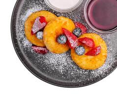 cabaña queso panqueques con bayas, en polvo azúcar, mermelada, y agrio crema en negro plato en blanco antecedentes foto