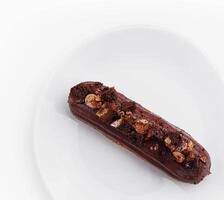 eclair with chocolate and nuts on a white plate photo