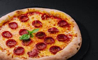 Pepperoni Pizza with Basil and Parmesan Cheese on Black Stone Plate photo