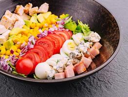 Bowl with chicken, egg, tomatoes, lettuce, corn, red onion and blue cheese photo