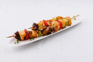 Grilled chicken skewers with vegetables on white plate photo