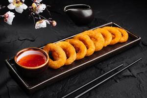 Crispy fried onion rings with dipping sauce on dark background photo