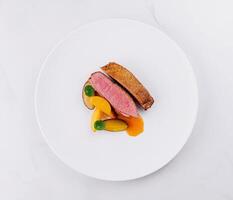 Gourmet duck breast with peach slices on white plate photo