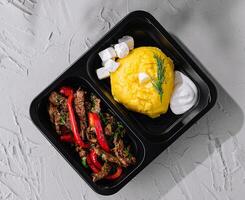 Takeout meal of beef stir-fry and polenta in black container photo