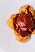 Gourmet profiteroles topped with rich chocolate sauce on a white plate photo