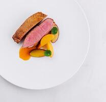 Gourmet duck breast with peach slices on white plate photo