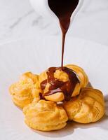 Pouring chocolate sauce over cream puffs on plate photo