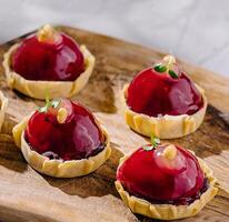 Elegant raspberry tarts on wooden board photo