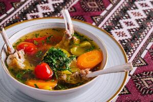 Traditional lamb soup with vegetables on patterned tablecloth photo