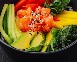 Fresh salmon poke bowl on dark background photo