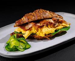 Delicious croissant sandwich with scrambled eggs, bacon, and avocado on a plate photo