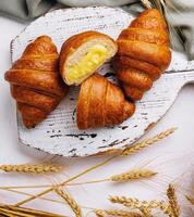 Fresh croissants on wooden cutting board with wheat ears photo