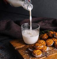 Pouring milk into glass beside freshly baked cookies photo