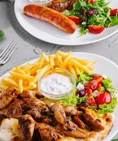 Delicious grilled chicken and sausage with fresh salad and fries photo