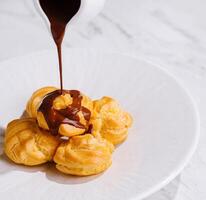 Pouring chocolate sauce over cream puffs on plate photo