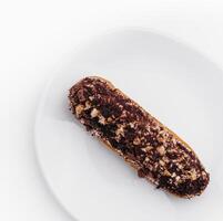 eclair with chocolate and nuts on a white plate photo