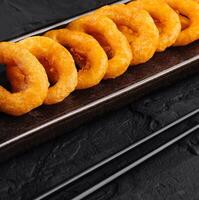 Crispy fried onion rings with dipping sauce on dark background photo