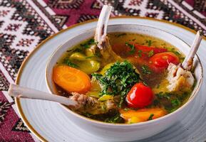 Traditional lamb soup with vegetables on patterned tablecloth photo