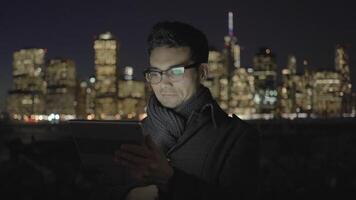 jovem ásia homem com óculos usando tábua tela computador dentro a cidade às noite video