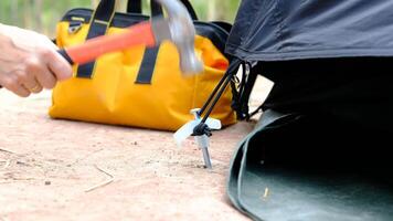 Tourists' hands use hammers to hammer into the ground to make the tents strong. video