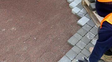 Worker Installing Pavement Blocks, A worker in orange safety gear carefully places interlocking pavement blocks on a freshly prepared base layer. video