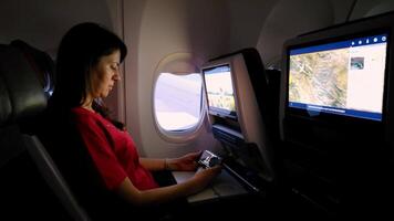 passager engagé avec en vol divertissement, une femelle passager en utilisant le en vol divertissement système pendant une vol, confortablement en train de regarder une film par le avion la fenêtre. video