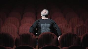 une homme est assis seul dans une chaise dans le génial salle de le opéra maison avec le sien yeux fermé. une rêveur solitaire homme dans une foncé salle avec rouge chaises. video