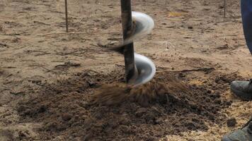 An auger drill is shown penetrating sandy soil und creating a hole . The activity takes place outdoors in a forested region. video