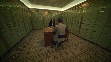 A man and a woman sit at a desk in a bank vault, creating a suspenseful scene video