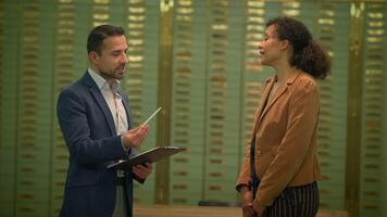 A man in a suit discusses financial matters with a woman in various settings, including a bank. The couple is seen conversing in a room and the man is seen holding a clipboard during a conversation video