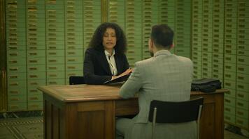 A man and a woman are sharing a wooden desk in a job interview room video