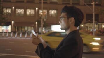 jong Aziatisch Mens met bril gebruik makend van tablet scherm computer in de stad Bij nacht video