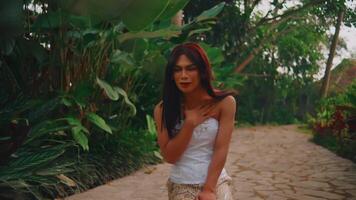 A woman in a white dress walking on a garden path surrounded by lush greenery, with a serene expression video