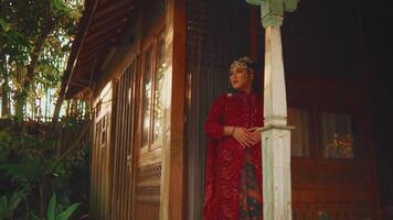 vrouw in traditioneel rood jurk staand in voorkant van een rustiek huis met groen. video