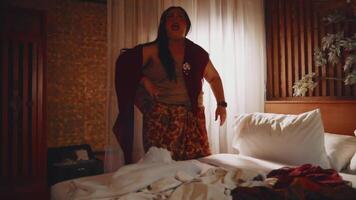 Woman standing by a bed in a dimly lit room, expressing surprise or shock. video