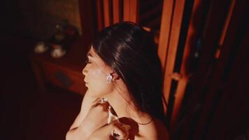 Elegant woman with diamond earrings looking away thoughtfully, warm indoor lighting video